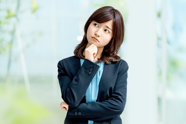 考え込む表情で腕を組むスーツ姿の女性